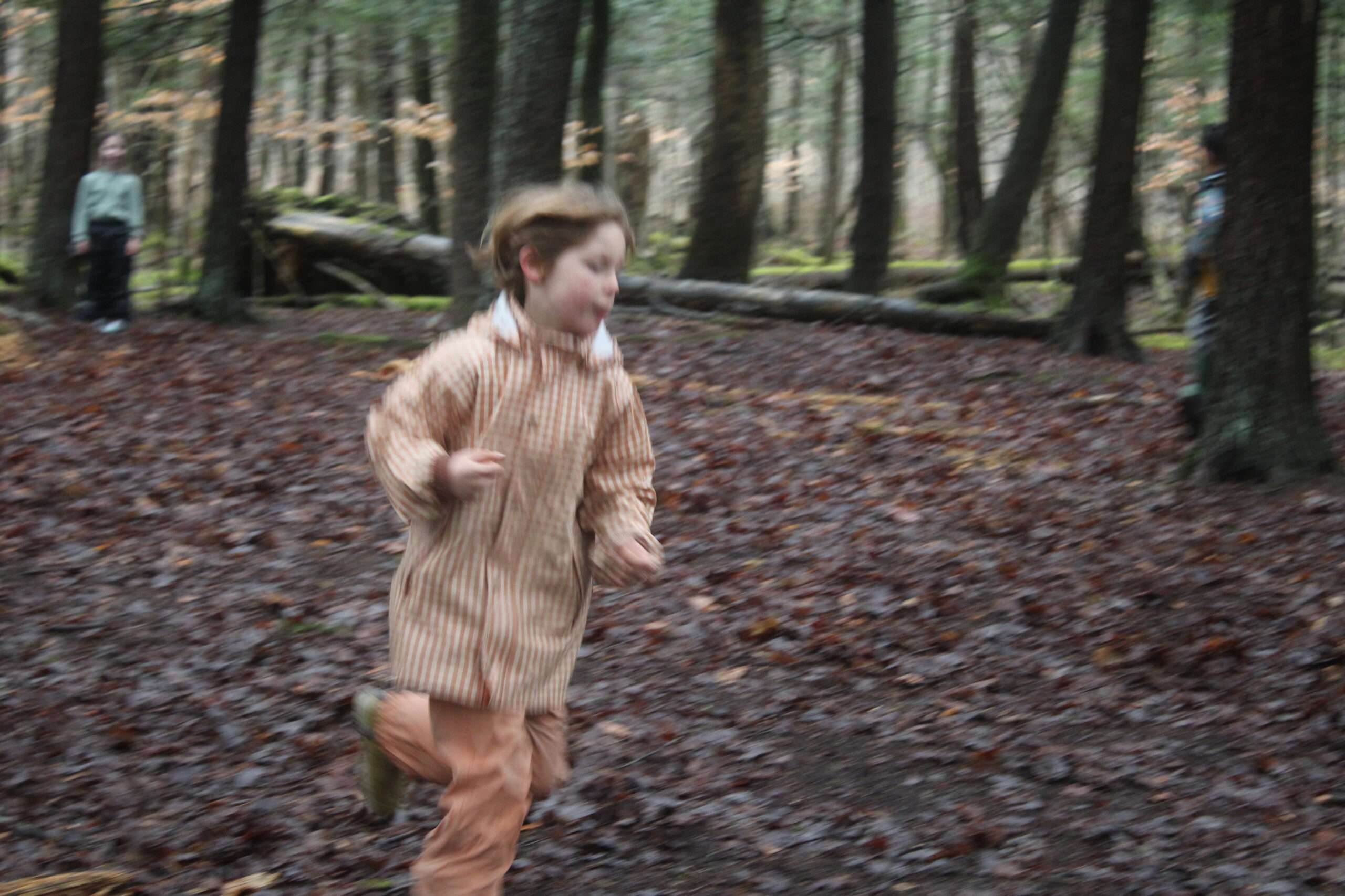 Young boy running through the woods playing.