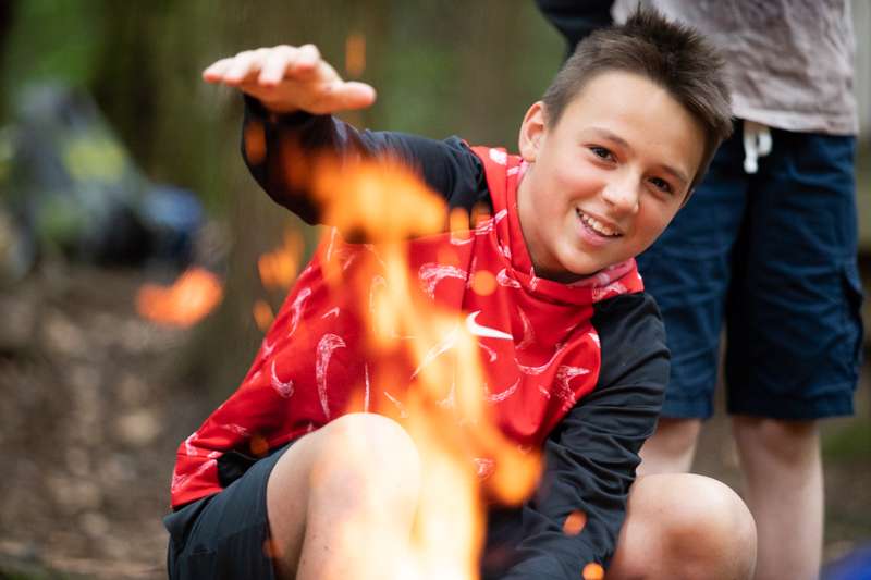 Young boy sitting by a campfire. 