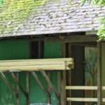 A green pavilion with a mossy roof in the woods.