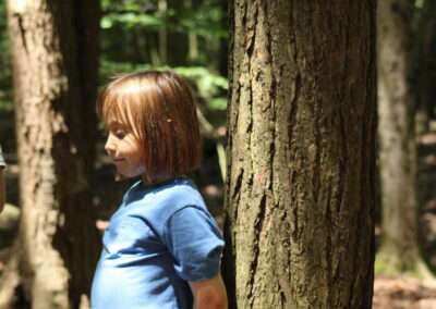 A young child lit up by the sun as they lean against a tree.