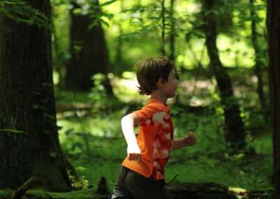 A young boy in an orange shirt running through the woods.