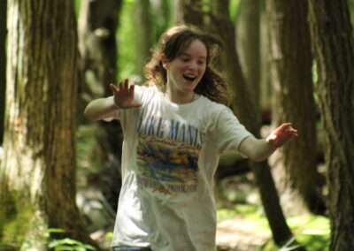 A smiling teenager with her hands up running through a leafy forest.