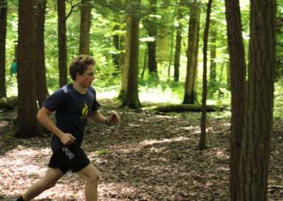 A teenager running through a green forest.