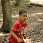 A young boy in a red shirt running through the forest.