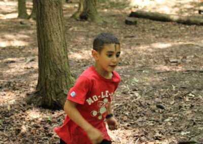 A young boy in a red shirt running through the forest.
