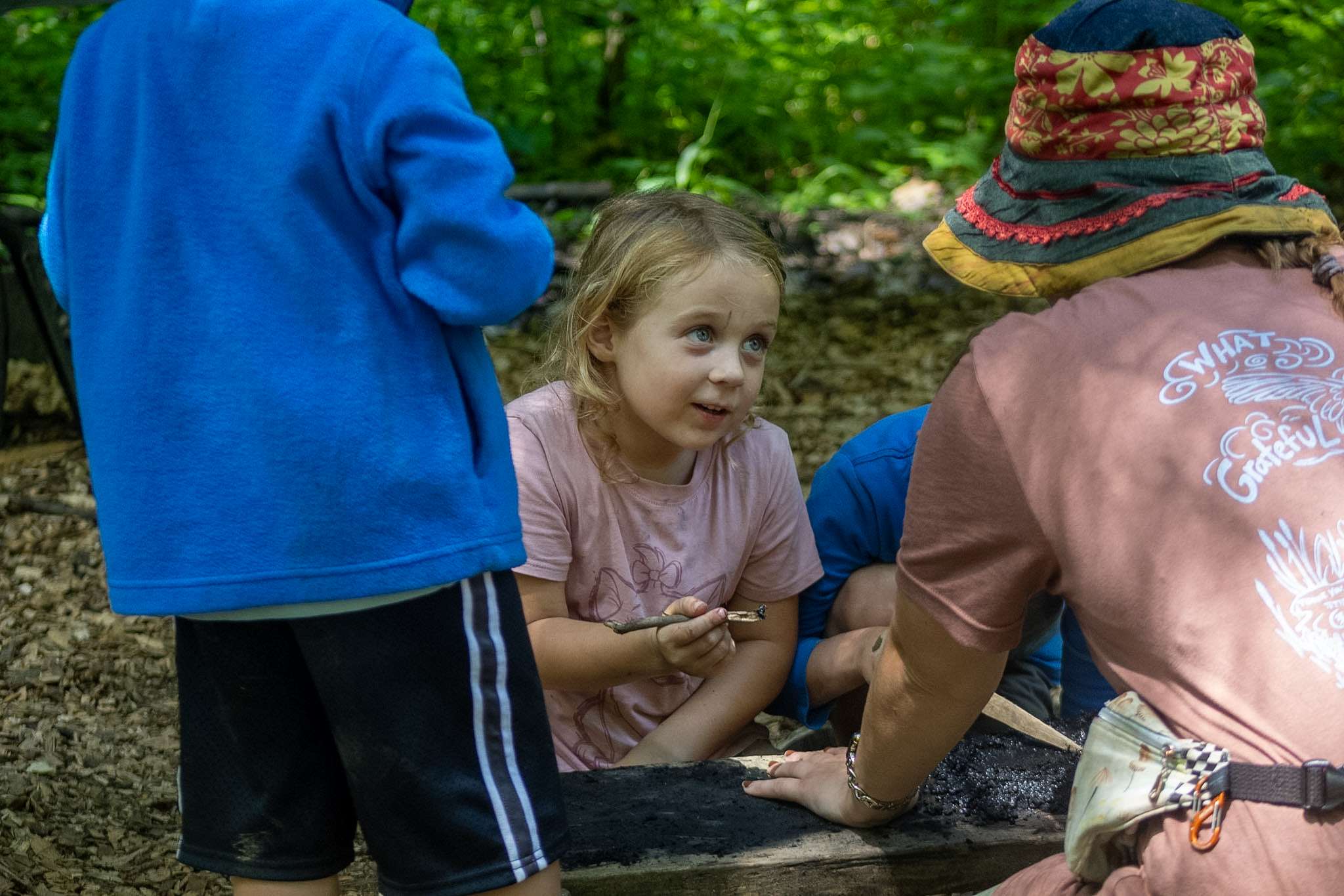 Camper holding stick with charcoal paint, interacting with an instructor and two other campers.