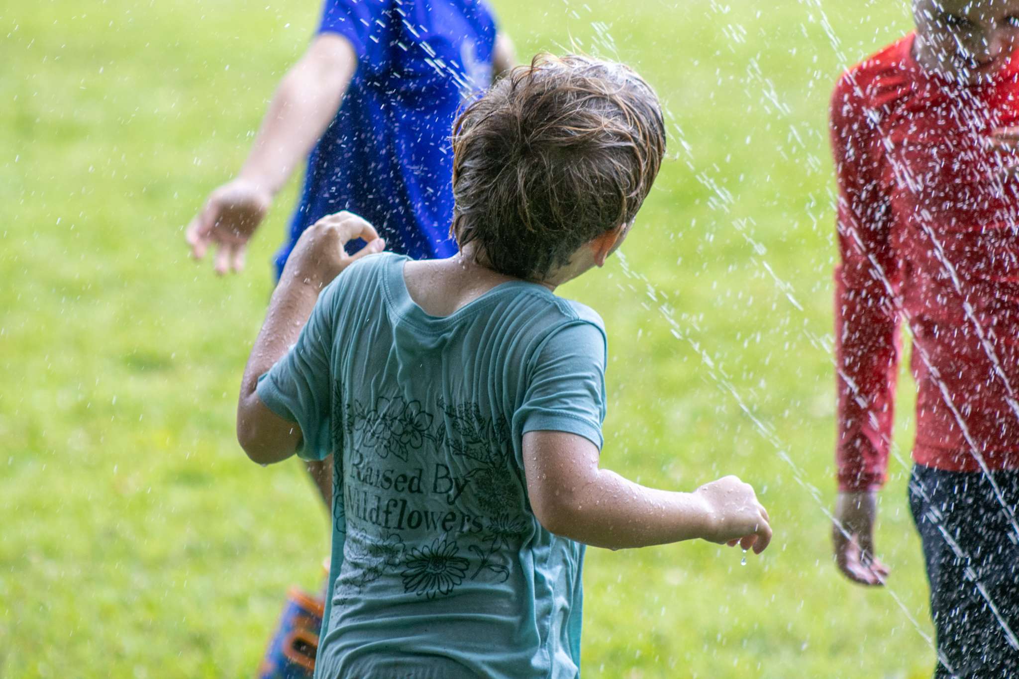 Younger camper standing in a sprinkler in the field.