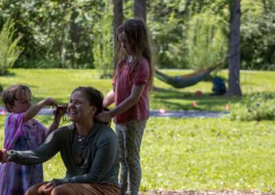 An instructor holding a campers hand while hair is being braided by two other campers.