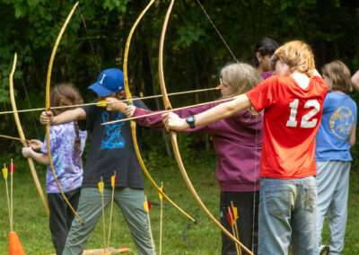 Four campers holding and aiming bows and arrows towards targets (not pictured).