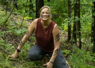 An instructor posing and smiling for the camera, with charcoal paint designs on her arms and face.