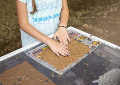 Hands smoothing out a brown paste to make paper.