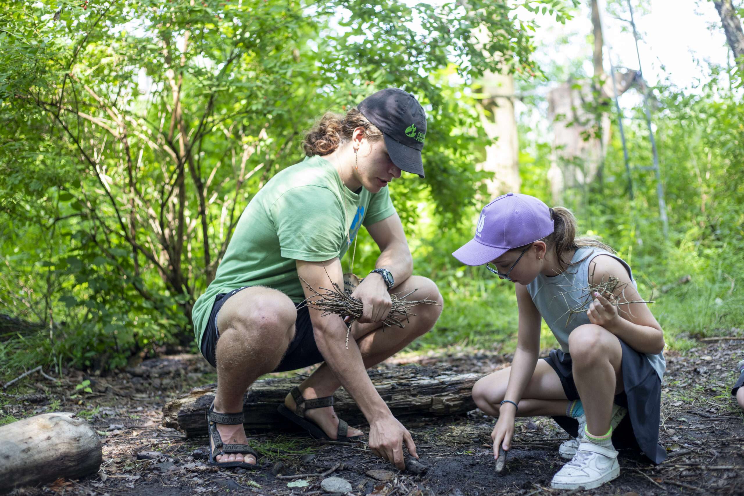 An instructor and a camper preparing a place to start a fire in the woods.