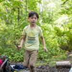 A young boy carrying sticks in the forest.