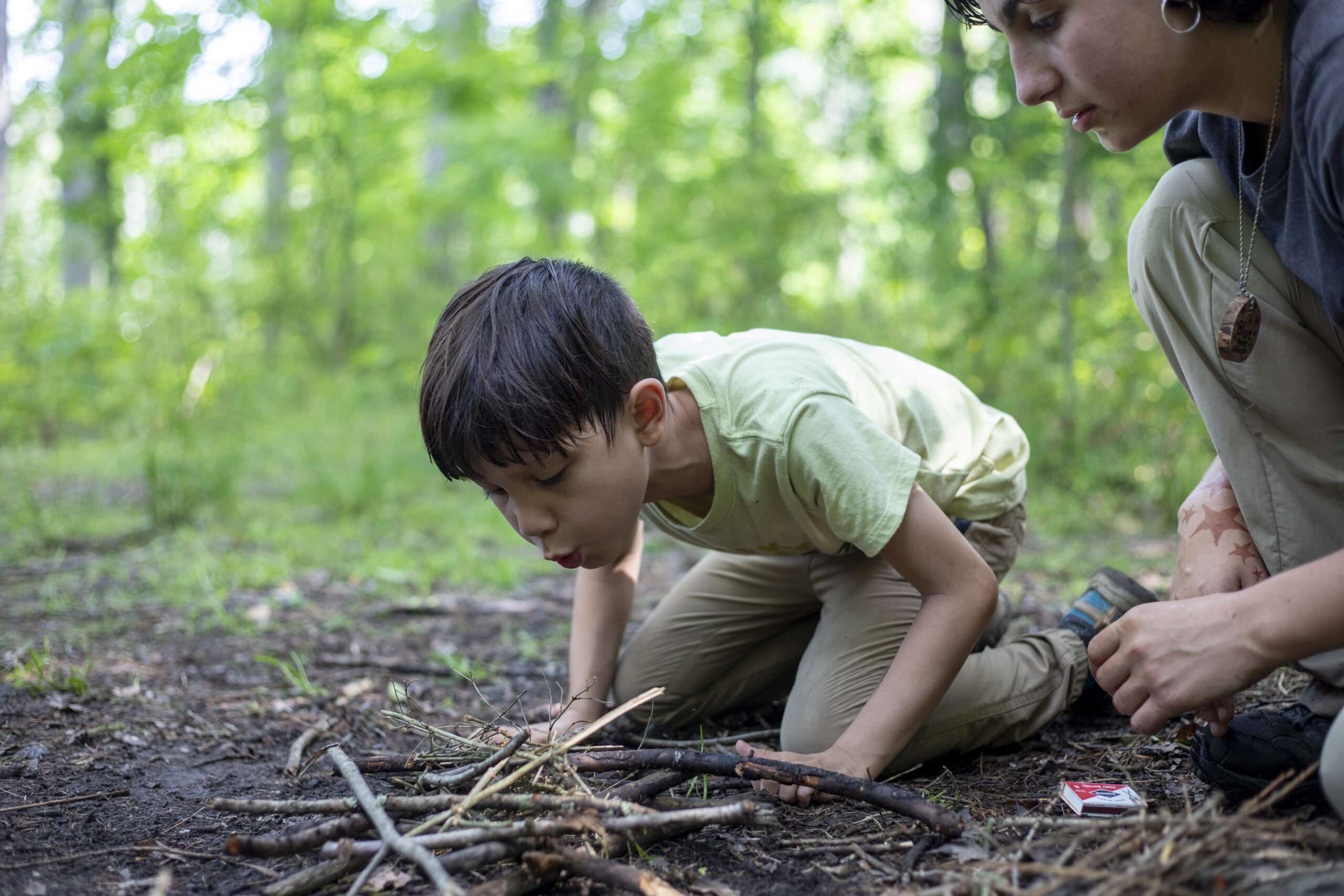 A camper and an instructor trying to start a fire in the woods.
