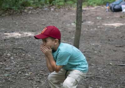 A younger camper holding his hands up to his mouth as he sneaks up on an instructor.