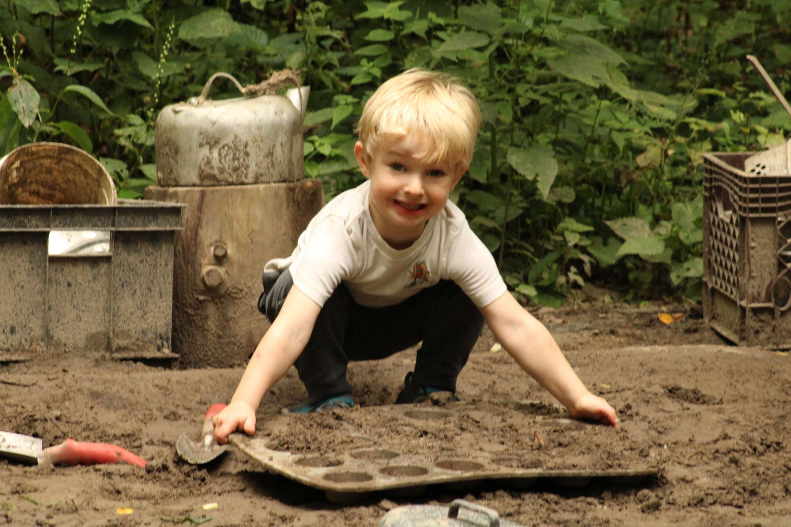 Younger camper holding a muffin tin filled with sand from the sandbox.