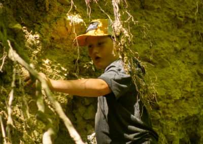An older camper using their hands to find clay in the side of a cliff.