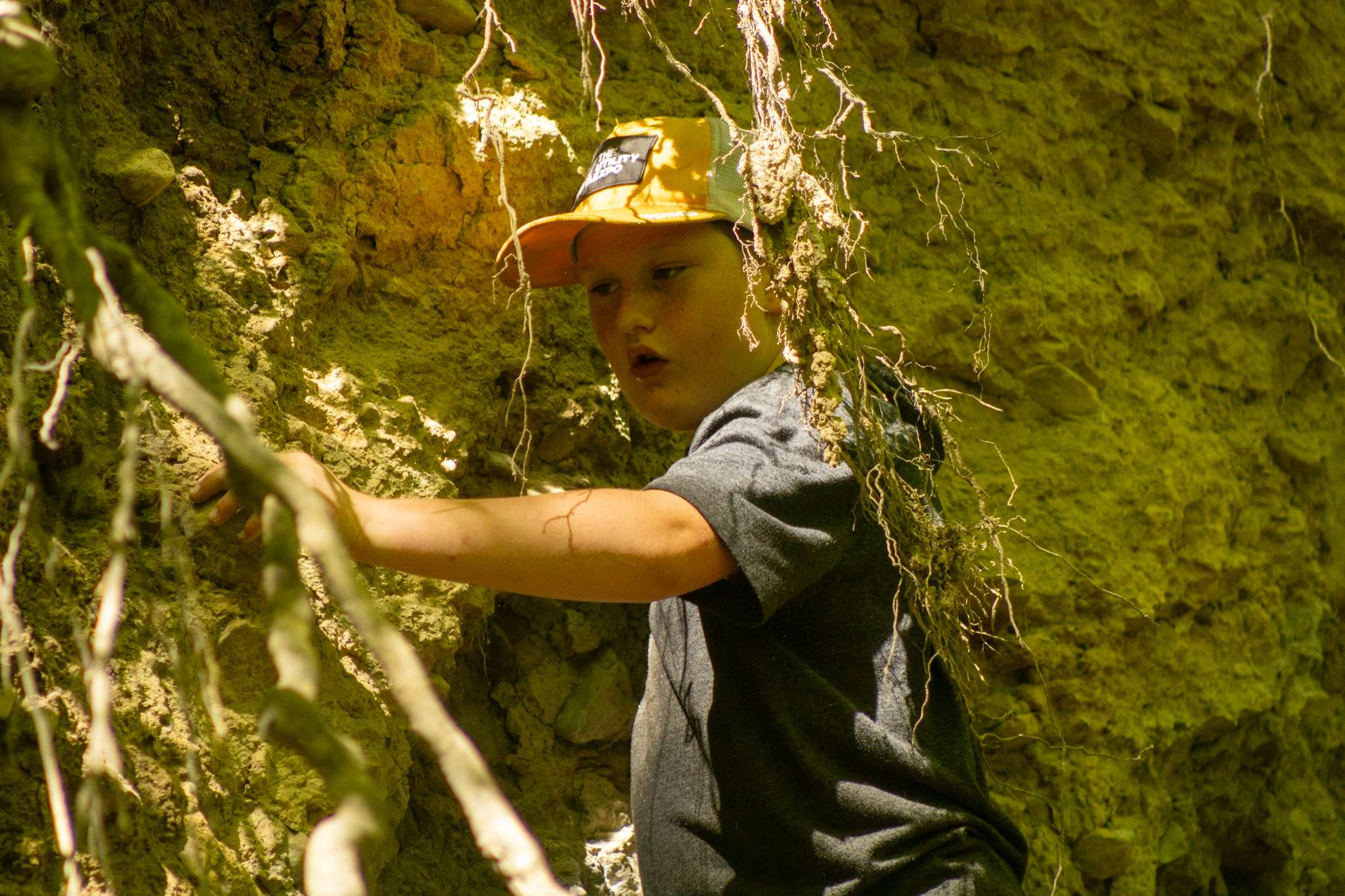 An older camper using their hands to find clay in the side of a cliff.