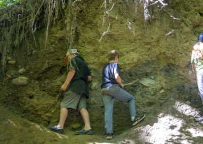 Two older campers standing against a cliff, searching for pieces of clay.