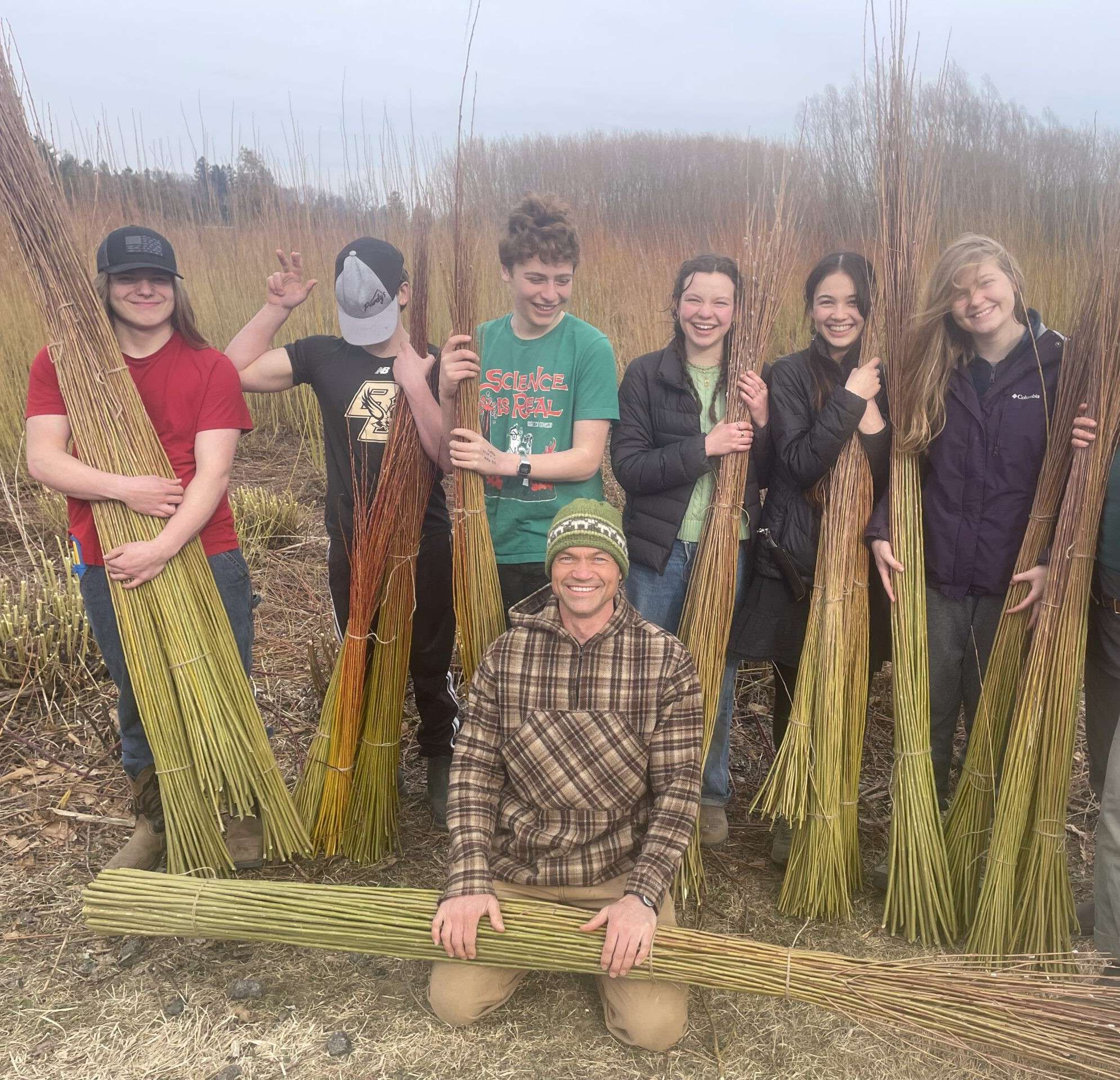 Group of 8 people, holding bundles of straw, smiling for the camera.